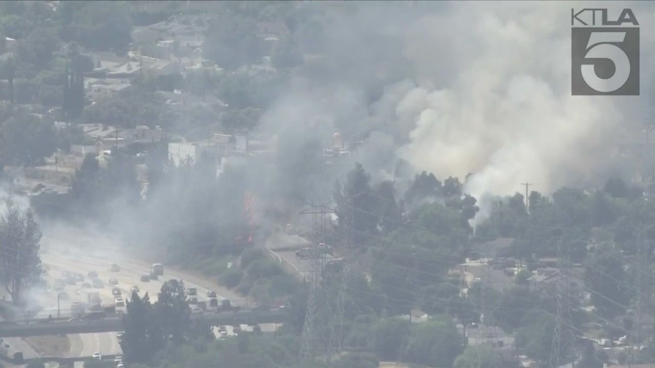 Los Angeles firefighters battle brush fire near freeway in Granada Hills